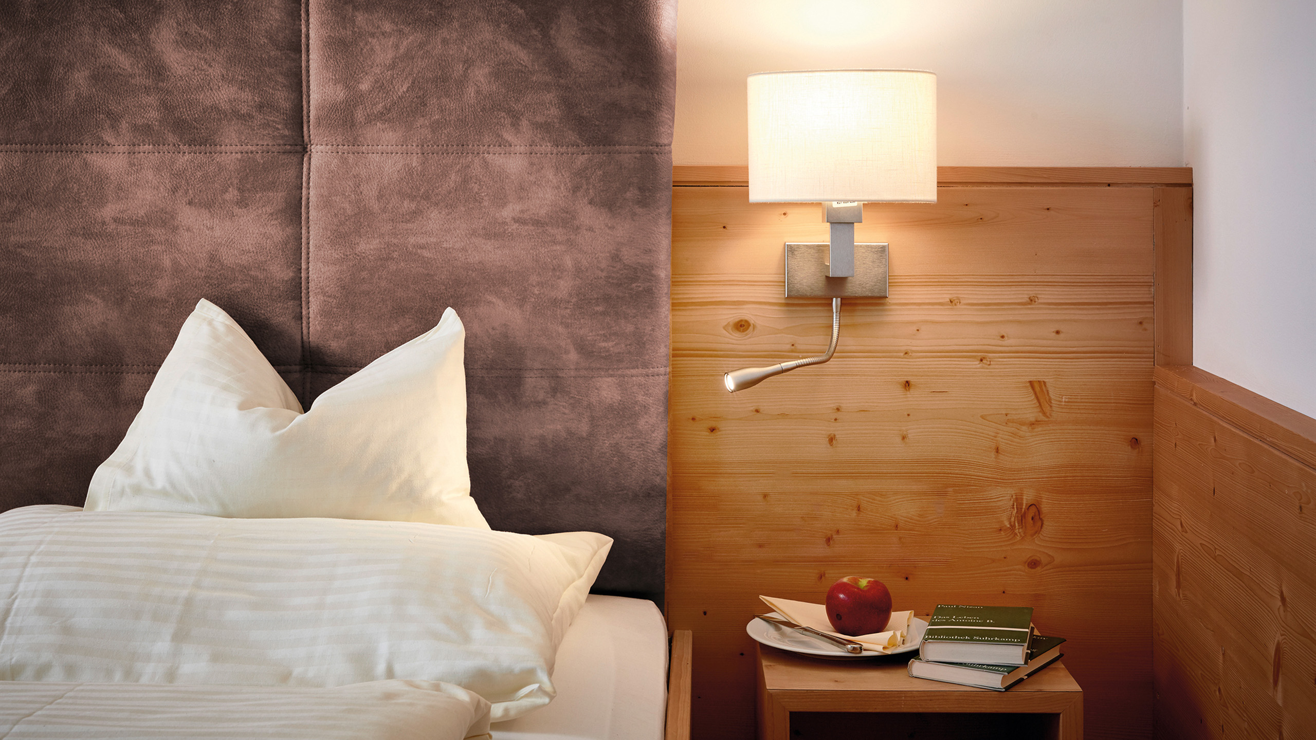 Gemütliches Hotelzimmer mit komfortablem Bett, Holzverkleidung und Nachttischlampe