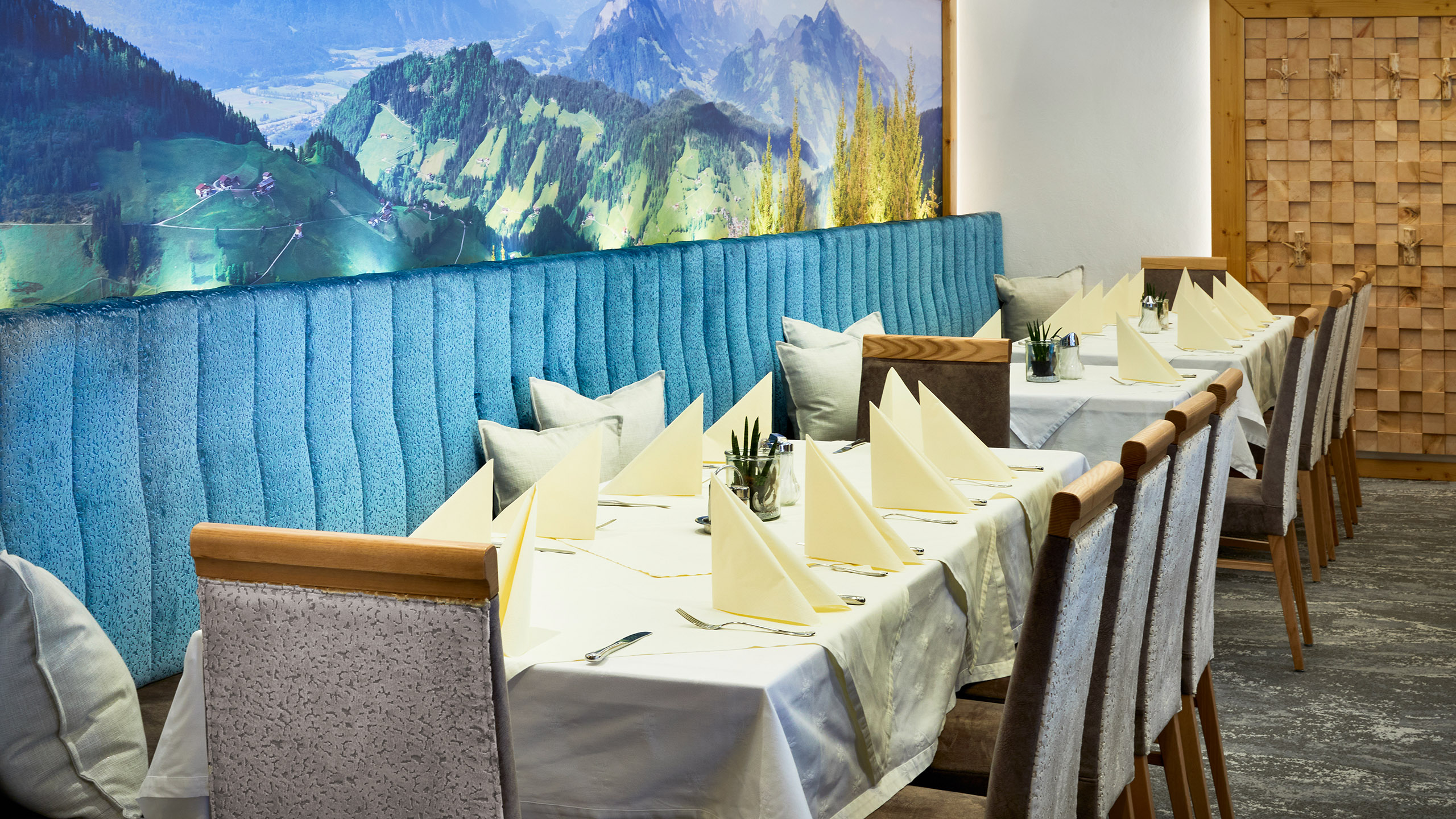 Gedeckter Restauranttisch vor gepolsterter Sitzbank und Alpenpanorama-Wandbild